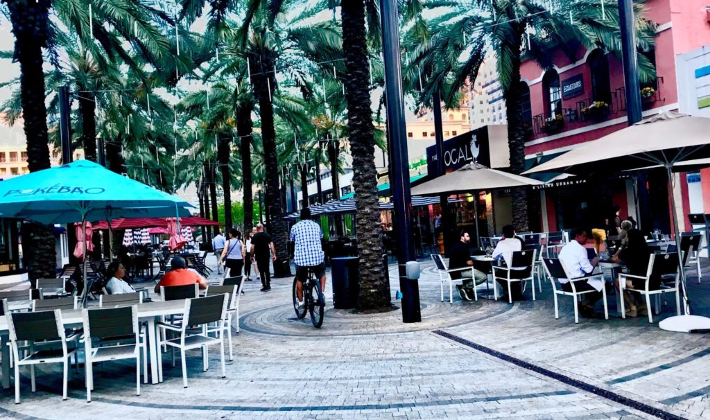 A photograph showing a lively pedestrian mall with outdoor dining tables and chairs in Florida. 