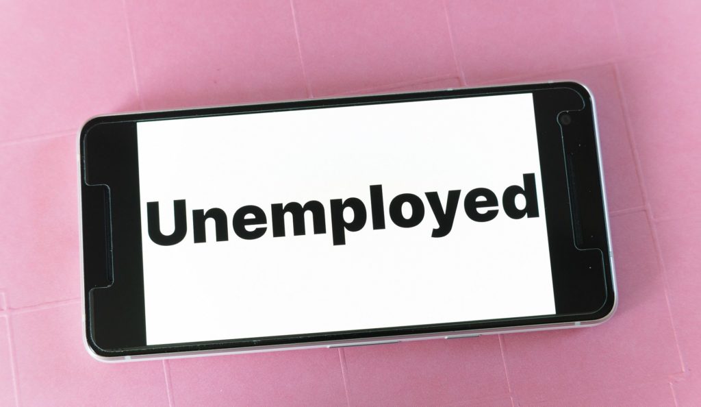 A photograph of a mobile phone with the word "Unemployed" displayed on the screen in black letters. Image by Markus Winkler from Pixabay. 