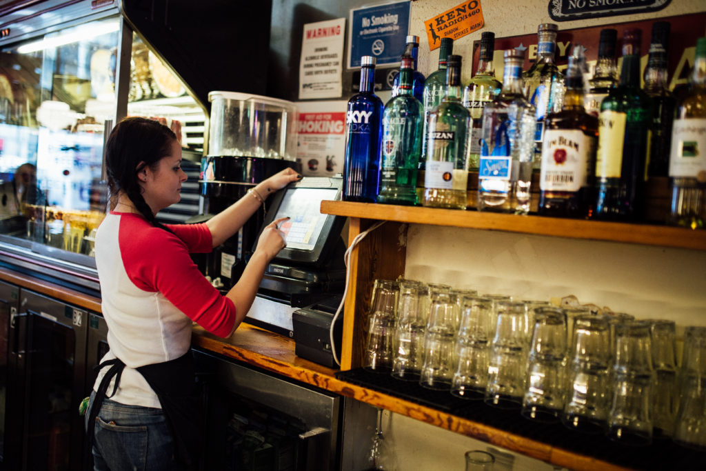 Photo of a server placing an order in a point of sale system behind a bar.  