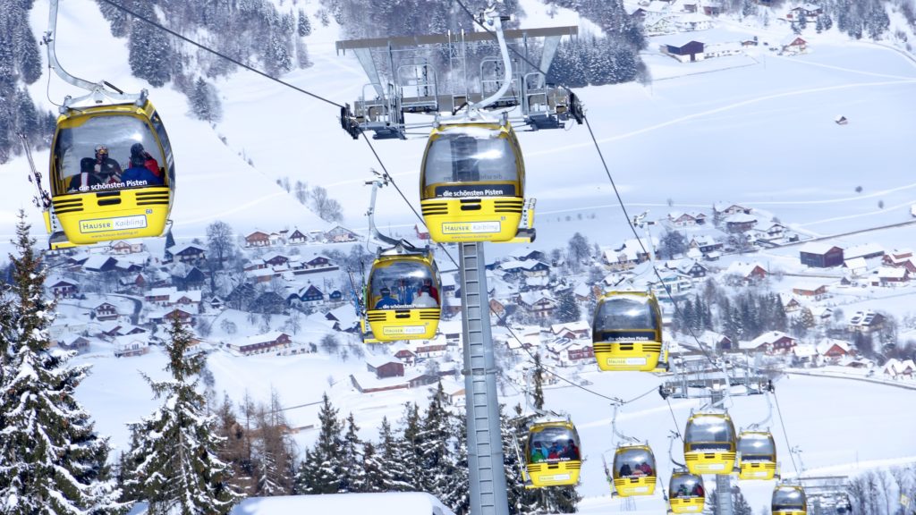 Photo of several yellow gondola cars going up the ski hill with a small, snowy town pictured in the background below. Photo by Boris Misevic on Unsplash. 