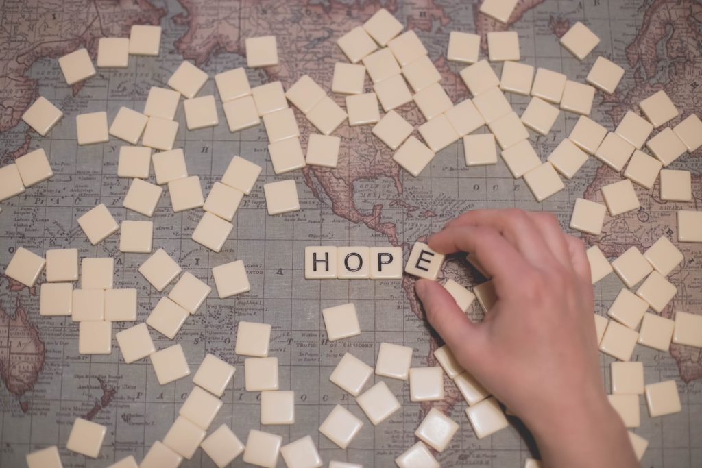 Photograph of a hand using Scrabble letter tiles to spell HOPE on a map of the world. Image credit: Dayne Topkin via Unsplash